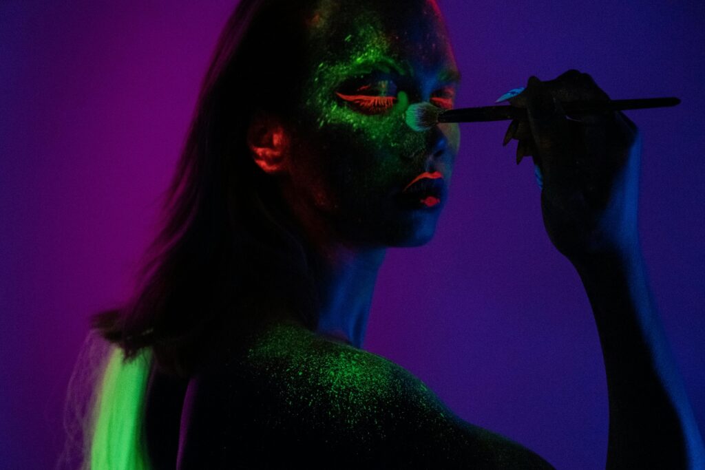 Artistic portrait with glowing makeup using fluorescent colors in low light.