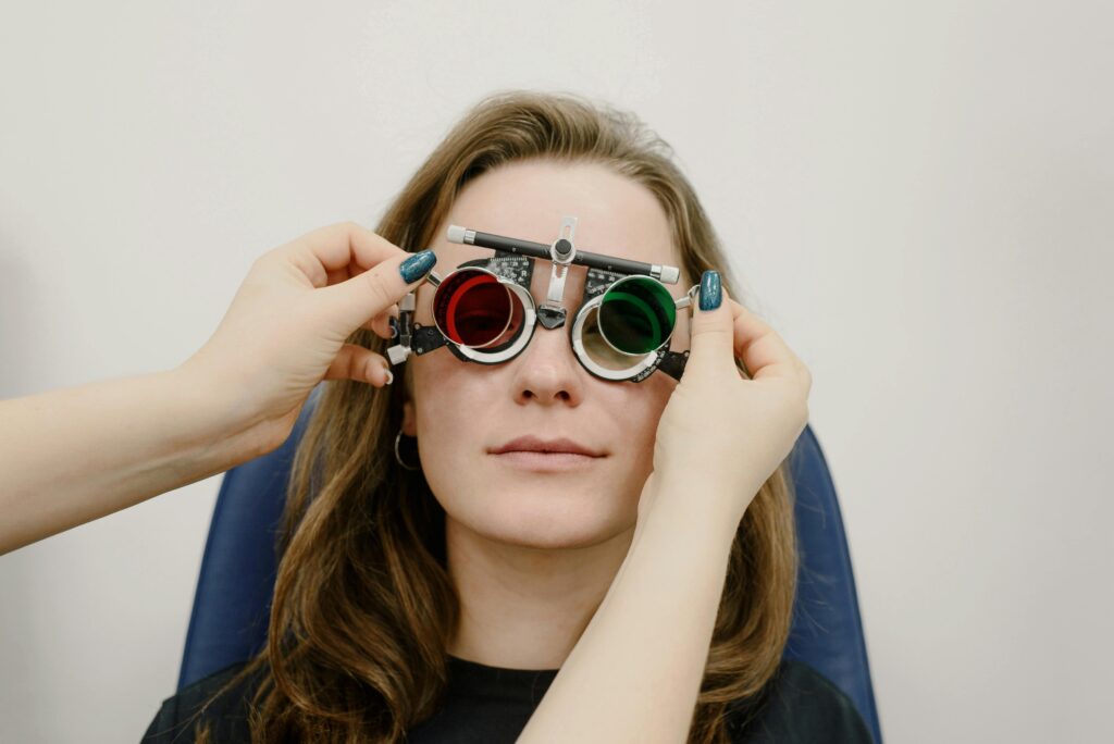 Unrecognizable female doctor correcting ophthalmic glasses selecting lenses on eyes of female patient during appointment in clinic against white wall
